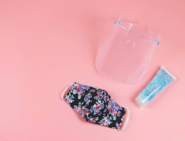 Coronavirus veya COVID-19 önleme ve yeni normal yaşam tarzı kavramı. Yüzün üst görünüşü, alkollü el dezenfektanı ve pembe arka planda çiçek desenli kumaş maskesi..