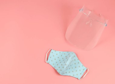 Coronavirus veya COVID-19 önleme ve yeni normal yaşam tarzı kavramı. Yüzün üst görünümü titrek ve pembe arkaplan üzerinde mavi benekli yüz maskesi kopyalama alanı ile.