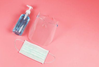 Coronavirus veya COVID-19 önleme ve yeni normal yaşam tarzı kavramı. Yüzün üst görünüşü, alkollü el dezenfektanı ve pembe arka planda cerrahi maske..