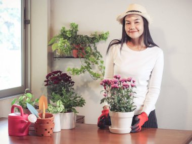 Güzel Asyalı kadın ahşap masada bitki yetiştiriyor, kameraya gülümsüyor..