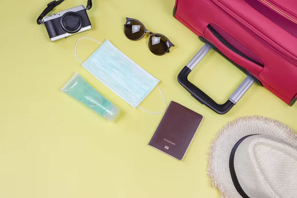 COVID-19 prevention while traveling and new normal lifestyle concept. Top view of surgical  face masks, alcohol  sanitizer gel and travel accessories on yellow background with copy space.