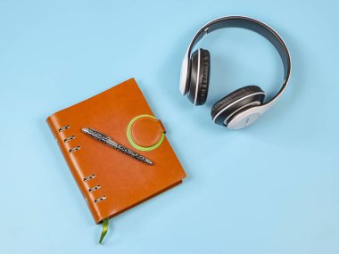 Mavi arka planda kalem ve beyaz kulaklıklı kahverengi defterin üst görünümü veya düz uzantısı.