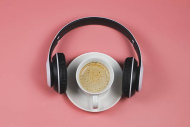 Üst ya da düz kulaklıklar ve pembe arka planda fotokopi alanı olan kahve fincanı. Müzik ve kahve rahatlama konsepti.