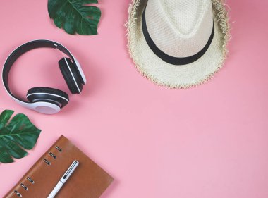 Rahatlatıcı zaman ve müzik kavramı. Pembe arka planda düz kulaklıklar, günlük ve şapka manzarası, tropikal canavar yapraklarıyla süslenmiş..