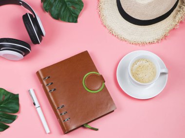 Kahve saati ve müzik konsepti. Kahve fincanının düzlüğü, kulaklıklar, pembe arka planda günlük ve şapka, tropikal canavar yapraklarıyla süslenmiş..