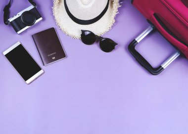 Gezgin aksesuarları, pasaport, şapka, cep telefonu, kamera, güneş gözlüğü ve mor arka planda pembe bavul. seyahat kavramı.