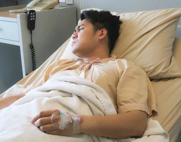 Asian young man  lying down in hospital bed , looking away.