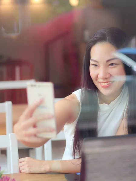 美丽的亚洲女人坐在咖啡店里开心地笑着 用手机自画像 — 图库照片