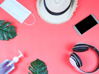 COVID-19 önleme ve yeni normal yaşam tarzı konsepti. Alkol dezenfekte edici el jeli ve hijyenik cerrahi yüz maskesi, kulaklık, şapka ve cep telefonlarının kırmızı arka planda üst görüntüsü.