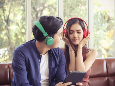 Çekici genç Asyalı çift evdeki kanepede kulaklık takıp müzik dinliyor.