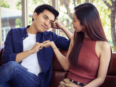 Oturma odasındaki kanepede oturan genç ve çekici çift. Bir erkek ve kız arkadaşının elleri birbirlerinin küçük parmaklarını birbirine kenetleyerek uzlaşır..