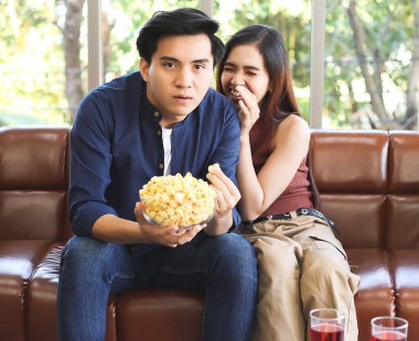 Çekici genç Asyalı çift oturma odasında kanepede oturup komik komedi filmleri seyrediyor. Elinde patlamış mısır tutan bir adam. Kız arkadaşı arkasına saklanıp gülüyor..