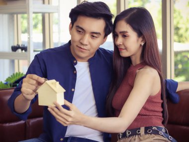 Çekici genç Asyalı çift, model evde yan yana otururken bir erkek model eve para koyuyor. Aile planlaması..