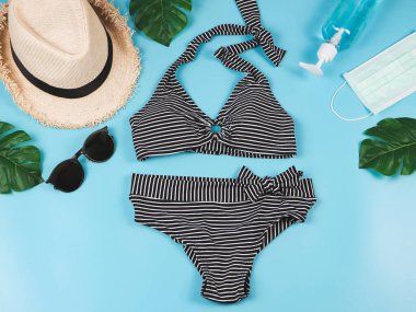 Yaz tatili ve yeni normal konsept, çizgili bikini mayo ve kadın tatil aksesuarları. Maskeli ve dezenfektan jöleli ve canavar yapraklı..