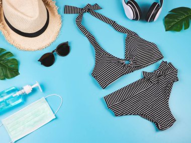 Yaz tatili ve yeni normal konsept, çizgili bikini mayo ve kadın tatil aksesuarları. Maskeli ve dezenfektan jöleli ve canavar yapraklı..