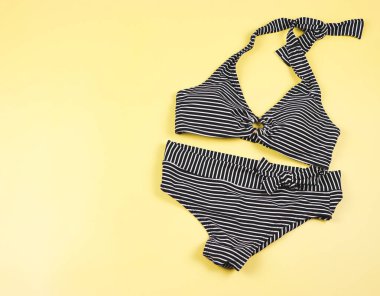 Yaz tatili kavramı. Üst manzara, düz alan, kopyalama alanı. Sarı arka planda siyah beyaz çizgili bikini mayosu. Kadın seksi mayo..