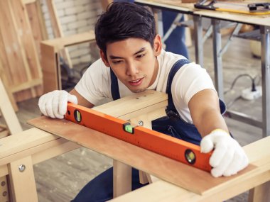 Asyalı genç ve yakışıklı marangoz su seviyesi ölçer kullanıyor. Odasında ahşap işçiliğiyle birlikte. Bir adamın yüzüne odaklanmış..