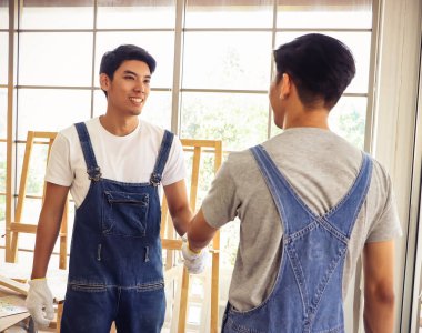 İki yakışıklı Asyalı tamirci ahşap atölyesinde el sıkışıyor ve işlerini bitirdikleri için seviniyorlar..