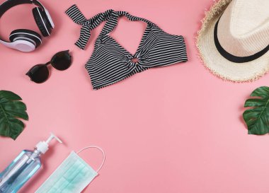 COVID-19 önleme, yaz ve yeni normal konsept, bikinili mayo ve kadın tatil aksesuarları cerrahi maske ve pembe arka planda canavar yapraklı dezenfektan..