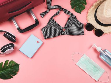 COVID-19 önleme, yaz ve yeni normal konsept, bikinili mayo ve kadın tatil aksesuarları cerrahi maske ve pembe arka planda canavar yapraklı dezenfektan..