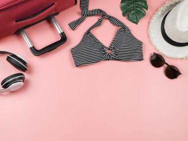 Yaz tatili kavramı. Üst manzara, düz alan, kopyalama alanı. Siyah beyaz çizgili bikini mayo bavulu ve pembe arka planda kadın tatil aksesuarları..