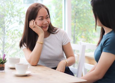 İki güzel Asyalı kadın kahve dükkanında oturup sohbet ediyor, bir kadın çenesiyle oturup diğer masada insanlarla dedikodu yapıyor.