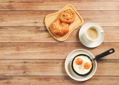 En iyi kahvaltı seti manzarası, tavada kızarmış yumurta, bir fincan kahve, Danimarka çöreği ve ahşap arka planda kruvasan..