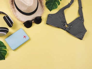 Seyahat ve yaz tatili konsepti, siyah beyaz çizgili bikini mayo, pasaport ve kadın tatil aksesuarları sarı arka planda tropikal canavar yapraklı..