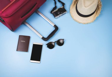 Gezgin aksesuarları, pasaport, şapka, cep telefonu, kamera, güneş gözlüğü ve mavi arka planda pembe bavul. seyahat kavramı.
