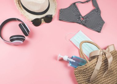 COVID-19 önleme, yaz ve yeni normal konsept, bikini yüzme kıyafetlerinin üst görünümü ve cerrahi maskeli kadın tatil aksesuarları ve pembe arka planda dokuma çantasında dezenfektan jeli..