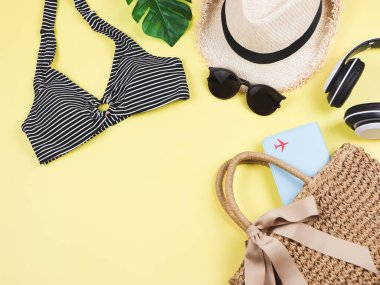 Seyahat ve yaz tatili konsepti, siyah beyaz çizgili bikini mayo, dokuma çantada pasaport ve sarı arka planda kadın tatil aksesuarları..