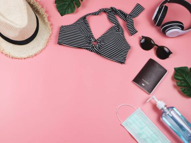 COVID-19 önleme, yaz ve yeni normal kavram, bikinili mayo ve pembe arka planda dezenfektan jeli kadın tatil aksesuarları..