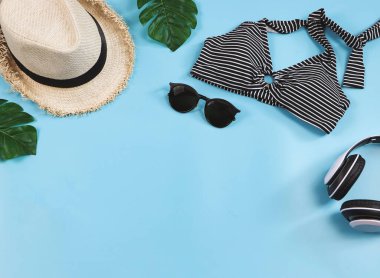 Seyahat ve yaz tatili konsepti, siyah beyaz çizgili bikini mayo ve mavi arka planda tropikal canavar yapraklı kadın tatil aksesuarları..