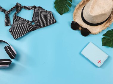 Seyahat ve yaz tatili konsepti, siyah beyaz çizgili bikini mayo, pasaport ve kadın tatil aksesuarları mavi arka planda tropikal canavar yapraklı..