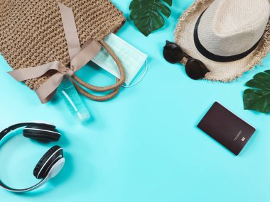 COVID-19 önleme, seyahat ve yeni normal konsept, cerrahi maskeli dokuma çantası, dezenfektan jeli, pasaport ve mavi arka planda kadın tatil aksesuarları.