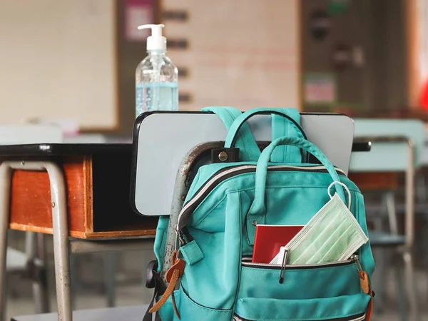 COVID-19 prevention , back  to school  and new normal  concept.School backpack with school supplies and medical face mask hanging with chair with alcohol gel on desk in classroom.