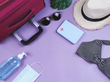 COVID-19 önleme, yaz ve yeni normal konsept, bikinili mayo ve kadın tatil aksesuarları, cerrahi maske ve mor arka planda dezenfektan jel.