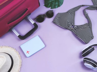 Seyahat ve yaz tatili konsepti, siyah beyaz çizgili bikini mayo, pasaport ve kadın tatil aksesuarları mor arka planda tropikal canavar yapraklı..