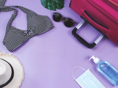 COVID-19 önleme, yaz ve yeni normal konsept, bikinili mayo ve kadın tatil aksesuarları, cerrahi maske ve mor arka planda dezenfektan jel.