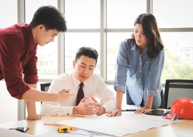 Üç inşaat işçisi, bir kadın mimar ve iki erkek mühendis ofis masasında projeyi tartışıyorlar..