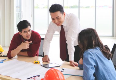 Üç inşaat işçisi, bir kadın mimar ve iki erkek mühendis ofis masasında projeyi tartışıyorlar..