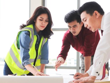 Üç inşaat işçisi, bir kadın mimar ve iki erkek mühendis ofis masasında projeyi tartışıyorlar..