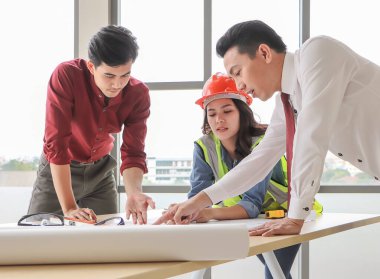 Üç inşaat işçisi, bir kadın mimar ve iki erkek mühendis ofis masasında projeyi tartışıyorlar..