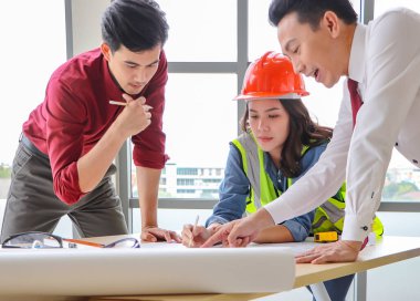 Üç inşaat işçisi, bir kadın mimar ve iki erkek mühendis ofis masasında projeyi tartışıyorlar..