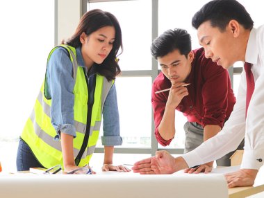 Üç inşaat işçisi, bir kadın mimar ve iki erkek mühendis ofis masasında projeyi tartışıyorlar..