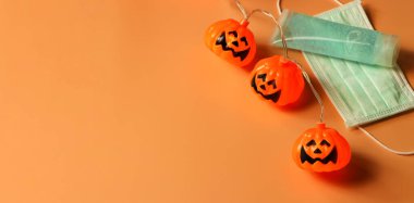 Cadılar Bayramı balkabağı ışıkları, tıbbi maske ve turuncu arka planda alkol dezenfektanı. Cadılar Bayramı, COVID-19 önleme ve yeni normal kavram.