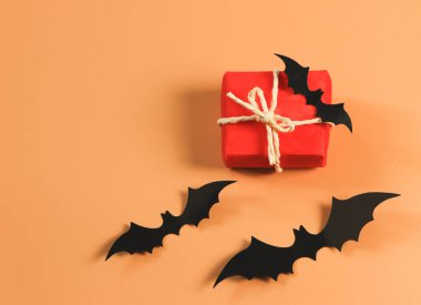 Kırmızı hediye kutusunun üstü ya da üstü turuncu arka planda siyah kağıt yarasalar ve fotokopi alanı ile kaplı. Cadılar Bayramı hediyesi kavramı.