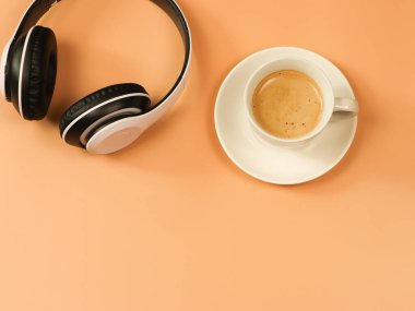 Üst ya da düz kahve yatağı ve turuncu arka planda kulaklık. Olumlu sabah, müzik ve ses konsepti..