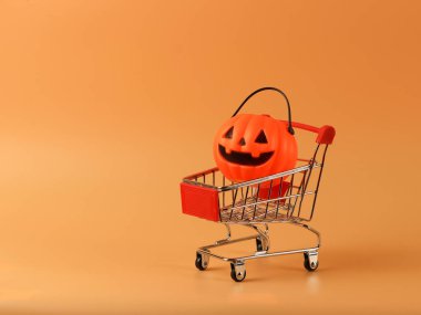 Fotokopi alanı olan turuncu arka planda alışveriş arabasında Cadılar Bayramı balkabağı manzarası. Cadılar Bayramı konsepti.