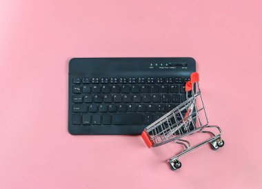 Pembe arka planda alışveriş arabası olan bilgisayar klavyesinin üst görünümü veya düz yatağı kopyalandı. Çevrimiçi konsept hoplatılıyor.